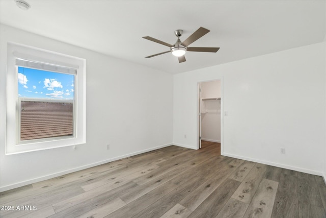 unfurnished bedroom with ceiling fan, a spacious closet, light hardwood / wood-style floors, and a closet