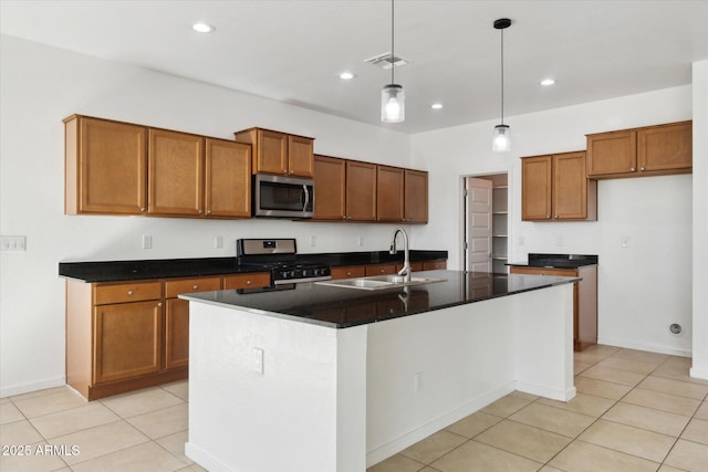 kitchen featuring light tile patterned flooring, sink, hanging light fixtures, stainless steel appliances, and a center island with sink