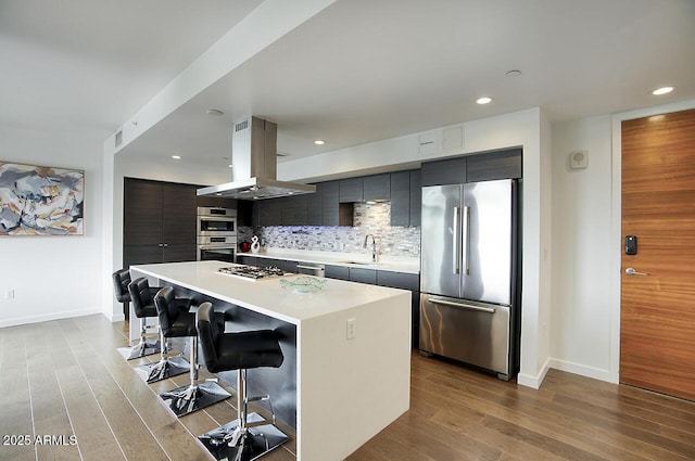 kitchen with a kitchen breakfast bar, island exhaust hood, backsplash, light wood-style floors, and appliances with stainless steel finishes