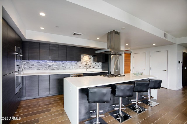 kitchen with a breakfast bar area, appliances with stainless steel finishes, modern cabinets, visible vents, and island range hood