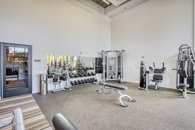 exercise room with baseboards and a towering ceiling