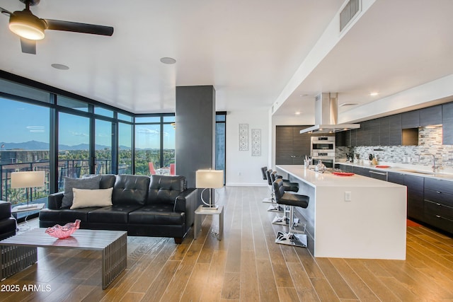 living room featuring expansive windows, light wood-type flooring, visible vents, ceiling fan, and a mountain view