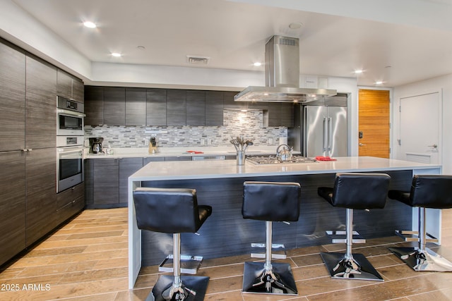 kitchen featuring visible vents, island exhaust hood, a breakfast bar, modern cabinets, and stainless steel appliances