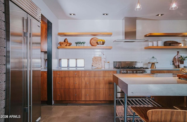 kitchen with high quality fridge, open shelves, light countertops, wall chimney exhaust hood, and brown cabinetry