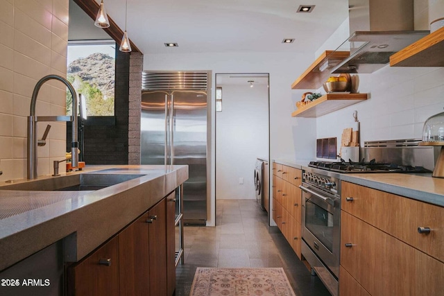 kitchen featuring premium appliances, decorative light fixtures, wall chimney range hood, open shelves, and a sink