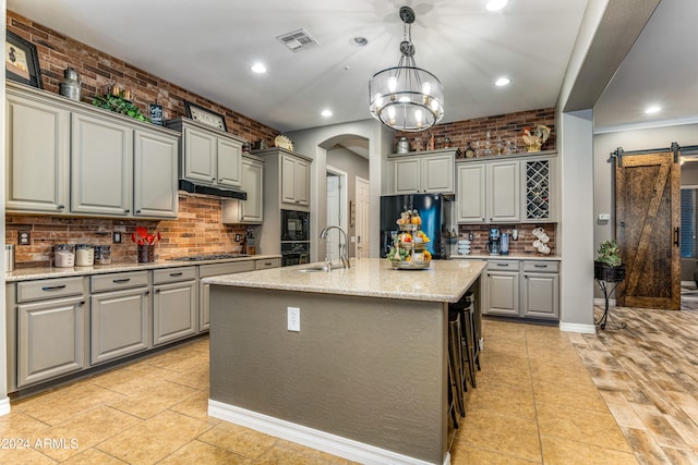 kitchen with a barn door, gray cabinets, a kitchen island with sink, and black appliances