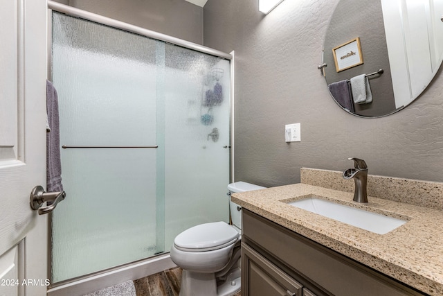 bathroom with hardwood / wood-style floors, vanity, a shower with door, and toilet