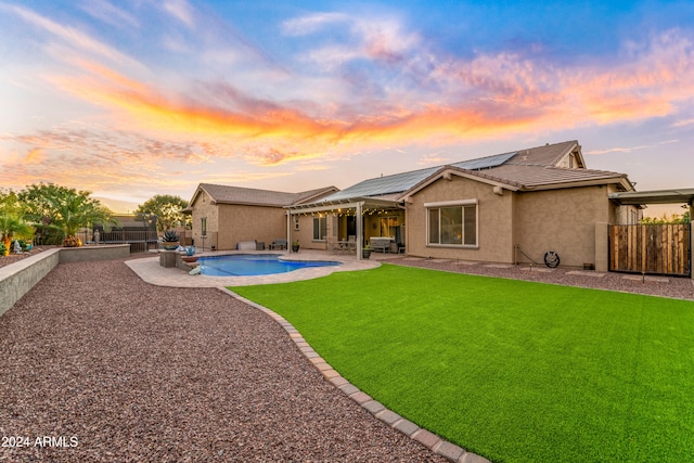 back house at dusk featuring a yard, a patio, a fenced in pool, and solar panels