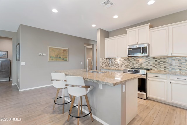 kitchen with appliances with stainless steel finishes, a sink, light wood-style flooring, tasteful backsplash, and visible vents