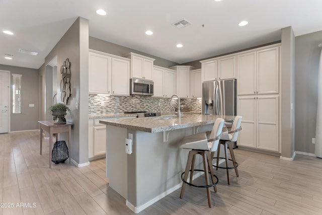 kitchen featuring decorative backsplash, stainless steel appliances, light wood finished floors, and visible vents