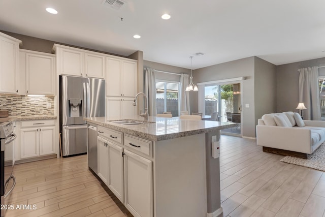 kitchen featuring visible vents, open floor plan, a sink, light wood-style flooring, and stainless steel appliances