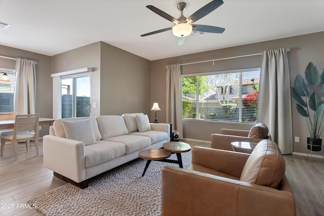 living area featuring baseboards, a ceiling fan, light wood finished floors, and a wealth of natural light