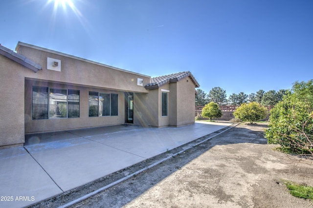 rear view of property featuring a patio area, fence, a tile roof, and stucco siding