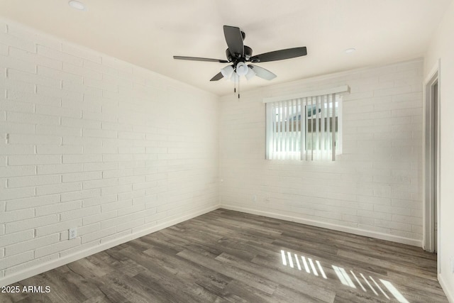 empty room with brick wall, baseboards, and dark wood-type flooring