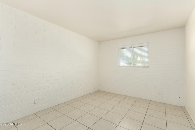 unfurnished room featuring light tile patterned floors and brick wall