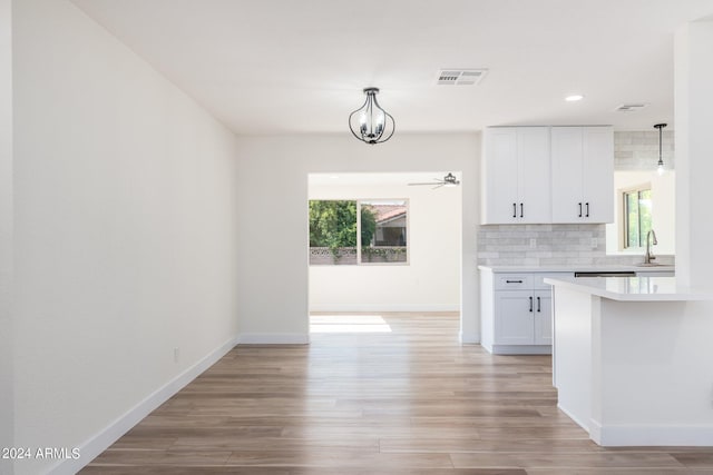 kitchen with pendant lighting, sink, white cabinetry, decorative backsplash, and ceiling fan with notable chandelier