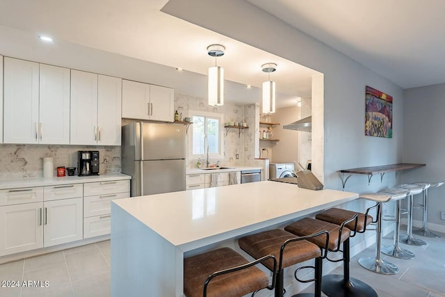 kitchen featuring appliances with stainless steel finishes, sink, white cabinets, hanging light fixtures, and a breakfast bar area