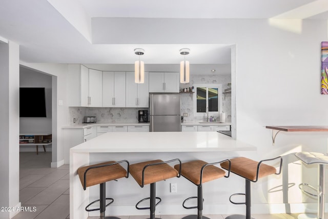 8301 E Crestwood Way, Scottsdale, AZ 85250 - kitchen with freestanding refrigerator, decorative backsplash, a breakfast bar, light countertops, and white cabinetry