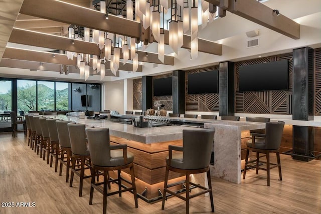 bar with a towering ceiling, beam ceiling, and light hardwood / wood-style flooring