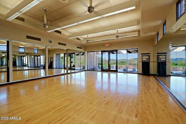 exercise area with ceiling fan, light wood-type flooring, and a towering ceiling