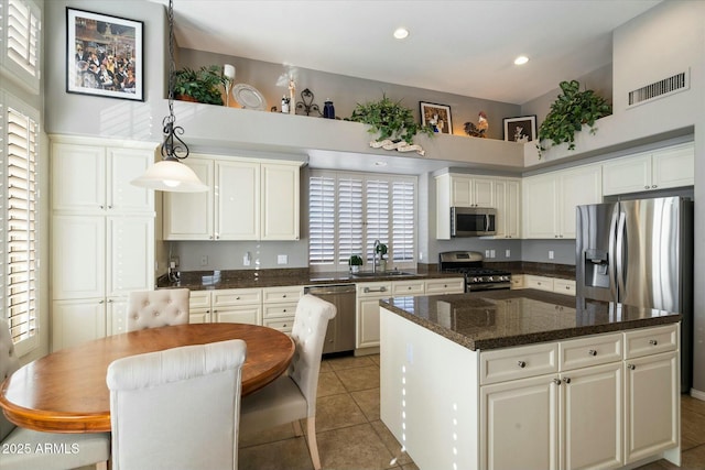 kitchen with pendant lighting, a kitchen island, light tile patterned floors, appliances with stainless steel finishes, and white cabinets