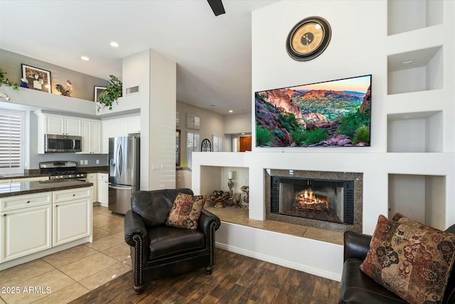 living room featuring light wood-type flooring, a towering ceiling, and a tile fireplace