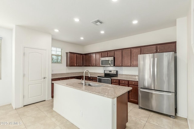 kitchen with a center island with sink, visible vents, light stone countertops, stainless steel appliances, and a sink