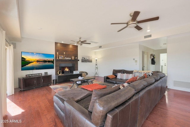 living room featuring dark wood-type flooring, a large fireplace, and ceiling fan