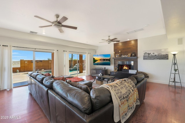 living room featuring ceiling fan, a large fireplace, and dark hardwood / wood-style floors