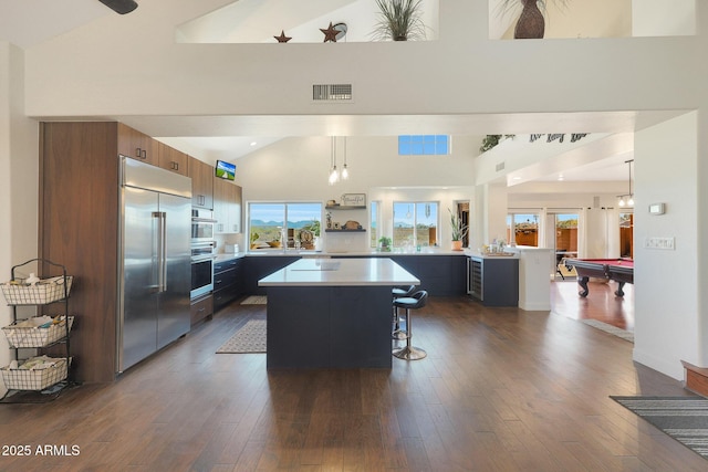 kitchen with a kitchen bar, appliances with stainless steel finishes, dark hardwood / wood-style floors, a kitchen island, and pendant lighting