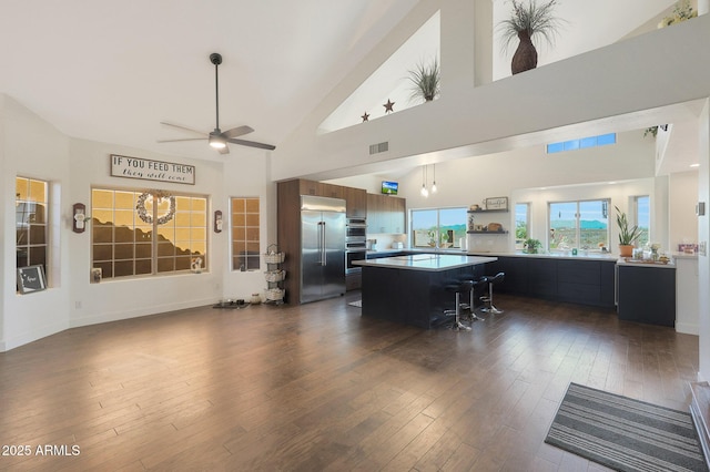 kitchen with a breakfast bar area, dark hardwood / wood-style flooring, a kitchen island, ceiling fan, and stainless steel appliances