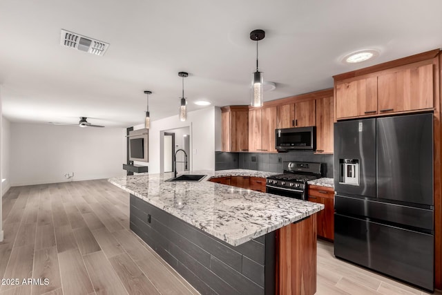 kitchen featuring sink, fridge with ice dispenser, hanging light fixtures, light wood-type flooring, and stainless steel range with gas stovetop