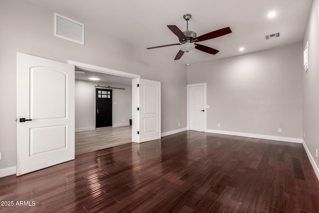 unfurnished living room with a high ceiling, ceiling fan, a barn door, and dark hardwood / wood-style flooring