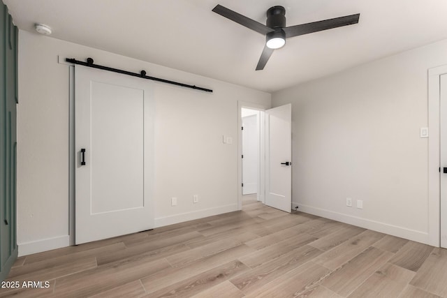 unfurnished bedroom featuring ceiling fan, a barn door, and light hardwood / wood-style flooring