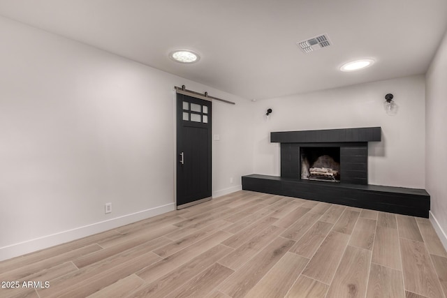 unfurnished living room with a barn door, a fireplace, and light hardwood / wood-style flooring