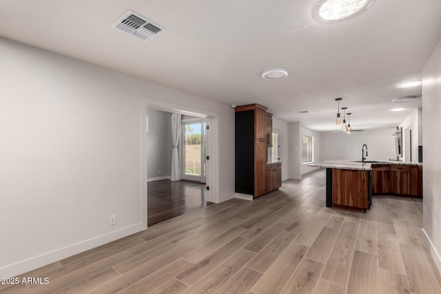 kitchen featuring sink, hanging light fixtures, light stone countertops, kitchen peninsula, and light wood-type flooring