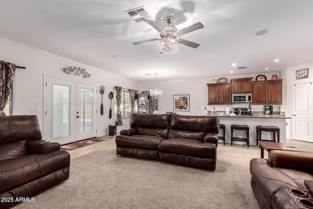 living room featuring light carpet, ceiling fan with notable chandelier, and french doors