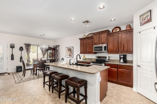 kitchen featuring a breakfast bar, sink, hanging light fixtures, a kitchen island with sink, and stainless steel appliances