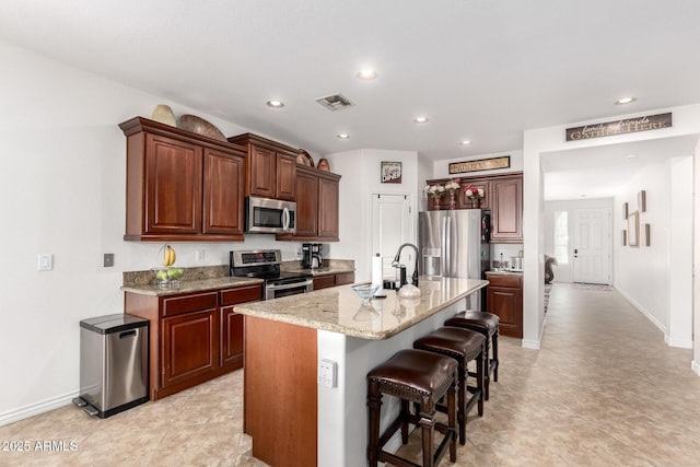 kitchen with sink, a breakfast bar area, appliances with stainless steel finishes, light stone counters, and a center island with sink