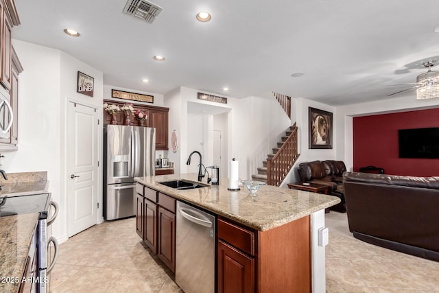 kitchen featuring sink, a kitchen island with sink, ceiling fan, light stone counters, and stainless steel appliances