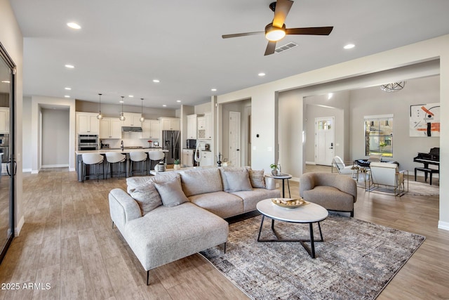 living room featuring sink, light hardwood / wood-style flooring, and ceiling fan