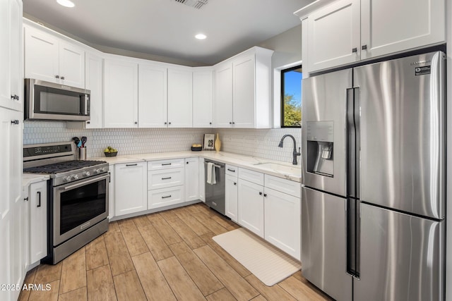 kitchen featuring sink, white cabinets, backsplash, stainless steel appliances, and light stone countertops