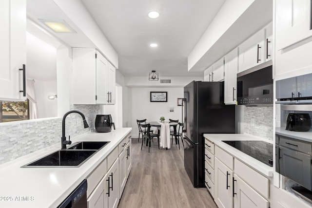 kitchen featuring tasteful backsplash, sink, white cabinets, black appliances, and light hardwood / wood-style flooring