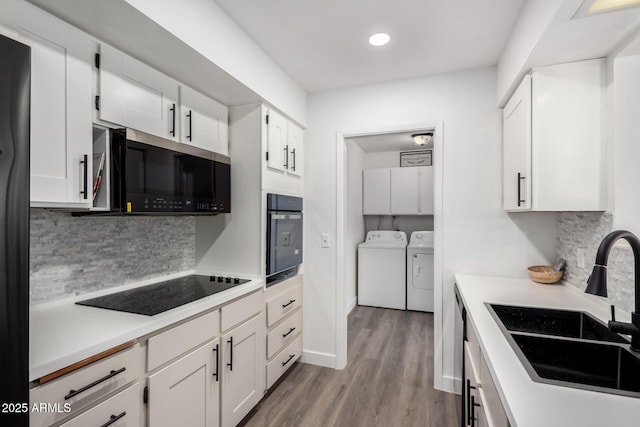 kitchen with sink, white cabinetry, black appliances, light hardwood / wood-style floors, and separate washer and dryer