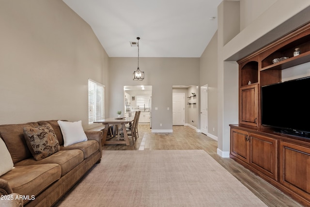 living area with light wood-style floors, baseboards, visible vents, and high vaulted ceiling