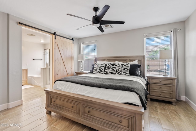 bedroom featuring visible vents, a barn door, baseboards, light wood finished floors, and ensuite bathroom