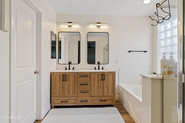 full bathroom with double vanity, a sink, a garden tub, and wood finished floors