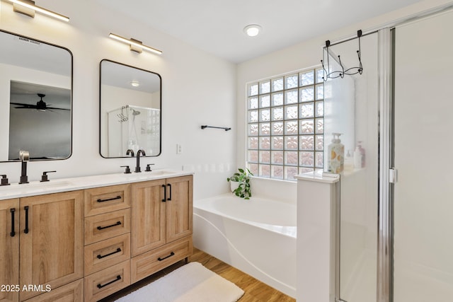 bathroom with ceiling fan, a sink, wood finished floors, a bath, and a stall shower