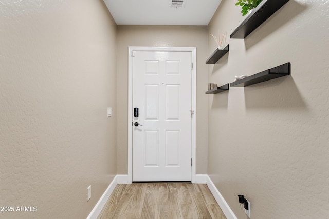 doorway with light wood-style floors, baseboards, and visible vents