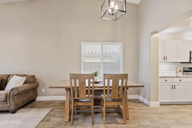 dining room with baseboards, a chandelier, light wood finished floors, and a towering ceiling